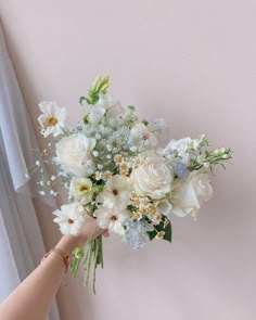 a person holding a bouquet of white and blue flowers in their hand next to a window