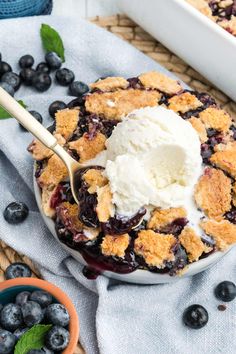 a blueberry cobbler with ice cream on top and fresh berries in the background