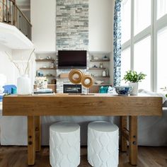 two white stools sitting under a wooden table in front of a tv mounted on the wall