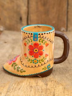 a coffee mug with a flower painted on it sitting on a wooden table next to a wall