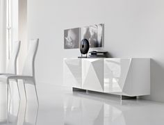 a white sideboard sitting on top of a white floor next to a vase and pictures