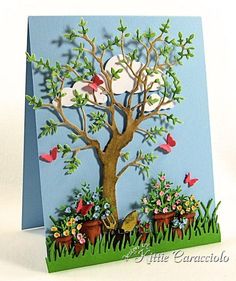 a handmade card with a tree and potted plants in the grass, on a blue background