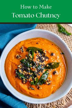 a white bowl filled with carrot hummus next to a blue napkin and green leafy garnish