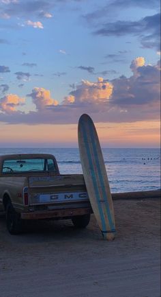 an old pickup truck with a surfboard leaning against it's bed on the beach