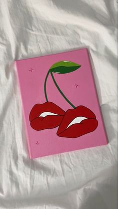 a pink canvas with two cherries painted on it, sitting on a white sheet