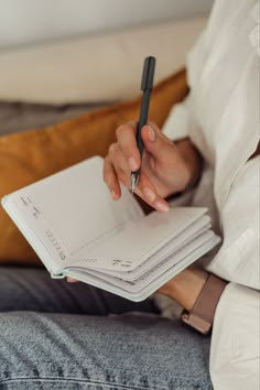 a person sitting on a couch holding a notebook and writing with a pen in their hand