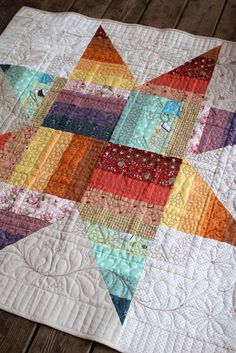 a multicolored star quilt on a wooden floor with the center piece being made