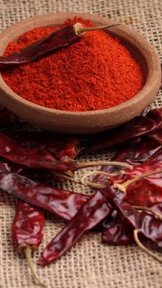 a bowl filled with red chili powder next to dried peppers