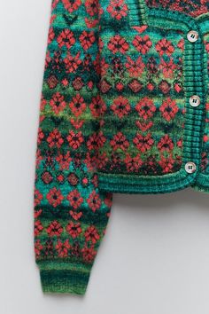 a green sweater with red and pink flowers on the front, sitting on a white surface