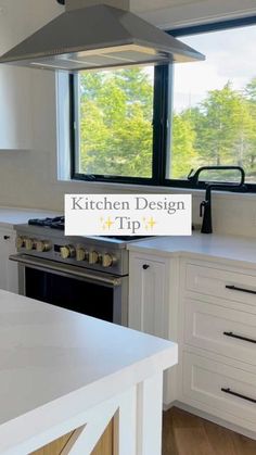 a kitchen with white cabinets and stainless steel range hood over the stove top, in front of a large window