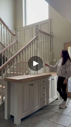 a woman standing in front of a kitchen counter next to a stair case and window