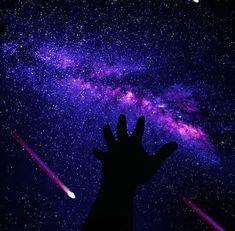 a person's hand reaching up to the sky with a bright purple and blue star in the background