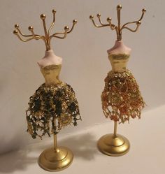 two mannequins made out of gold colored material and beads are standing on stands