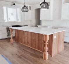 an island in the middle of a kitchen with two pendant lights hanging over it's head