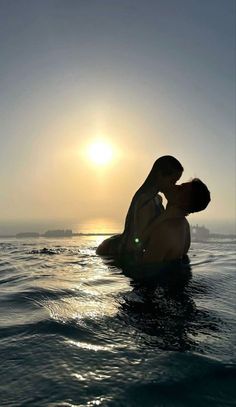 two people are sitting in the water with their backs to each other as the sun sets