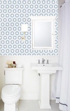 a white toilet sitting next to a sink in a bathroom under a mirror and shower curtain