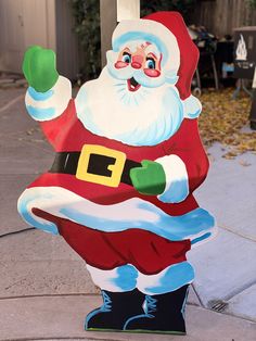 a large santa clause standing on top of a sidewalk next to a street sign with his hand in the air