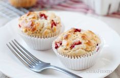 two muffins on a white plate with a fork and cupcake in the background