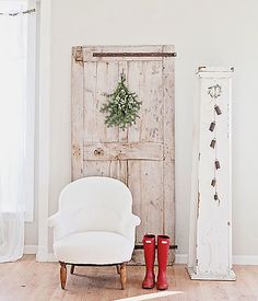 a white chair sitting in front of a wooden door next to two tall red boots