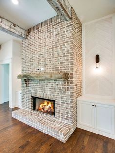 a brick fireplace in the middle of a room with wood flooring and white walls