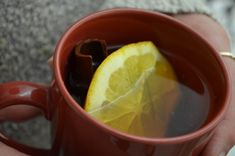 a person holding a red mug filled with tea and lemon wedged into the cup