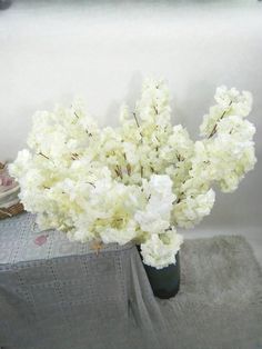 white flowers are in a vase on a gray table cloth next to books and a framed photograph