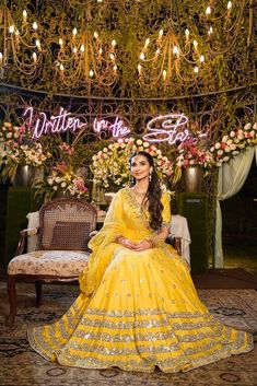 a woman in a yellow gown sitting on a chair under a chandelier with flowers