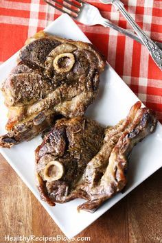 two steaks on a white plate with fork and knife next to them, sitting on a red checkered tablecloth