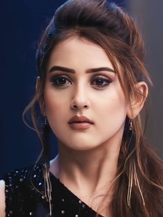 a woman with long hair wearing black dress and large hoop earrings on her head, looking at the camera