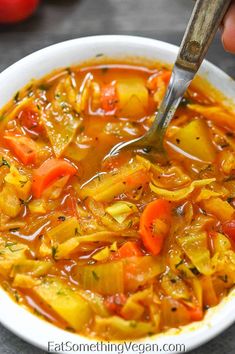 a person holding a spoon in a bowl of vegetable soup with carrots and onions