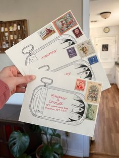 a person holding up some stamps on top of a piece of paper in front of a potted plant