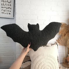 a woman is holding up a black bat pillow