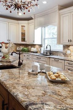 a large kitchen with marble counter tops and white cabinets, along with a chandelier hanging from the ceiling