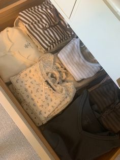 an open drawer filled with baby clothes on top of carpeted floor next to wall