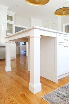 an island in the middle of a kitchen with wooden floors and white cabinets on both sides