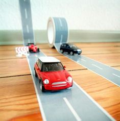 a toy car driving down a road with two cars on the opposite side of it