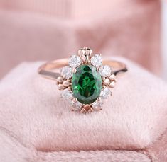 a ring with an oval green stone surrounded by small white diamonds on a pink blanket