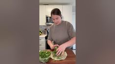 a woman cutting up lettuce on top of a wooden table in a kitchen