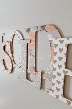 the word love spelled with wooden letters on a white wall next to flowers and hearts