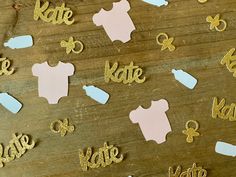 baby clothes and name cutouts are displayed on a wooden surface with gold glitters