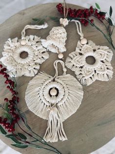 three white tasselled ornaments on top of a wooden table next to berries and greenery