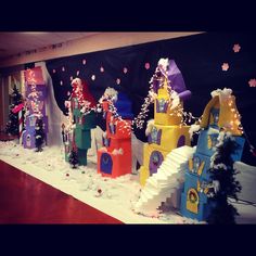 a group of colorful buildings sitting on top of a snow covered floor next to a christmas tree