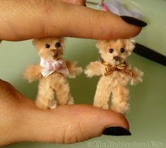 two tiny teddy bears are being held by someone's hand