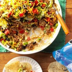 a large bowl filled with taco salad next to tortilla chips on a wooden table