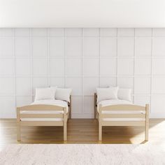 two beds sitting next to each other on top of a hard wood floor covered in white pillows