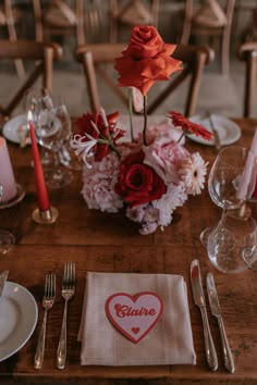 a wooden table topped with plates and silverware next to a vase filled with flowers