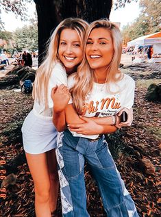 two girls hugging each other in front of a tree