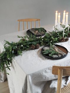 the table is set with pine cones, greenery and candles