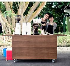 a man and woman standing behind a coffee cart