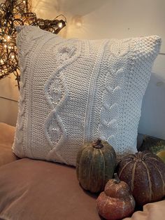 a white knitted pillow sitting on top of a bed next to two pumpkins